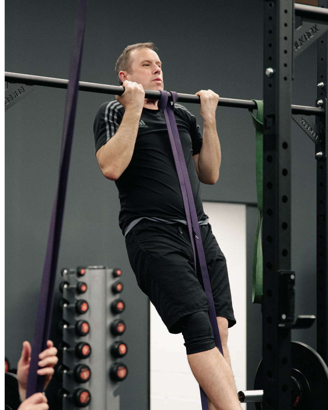 Middle-aged man performing a supported banded pull-up in a Gateshead gym, building strength during a coached fitness session.