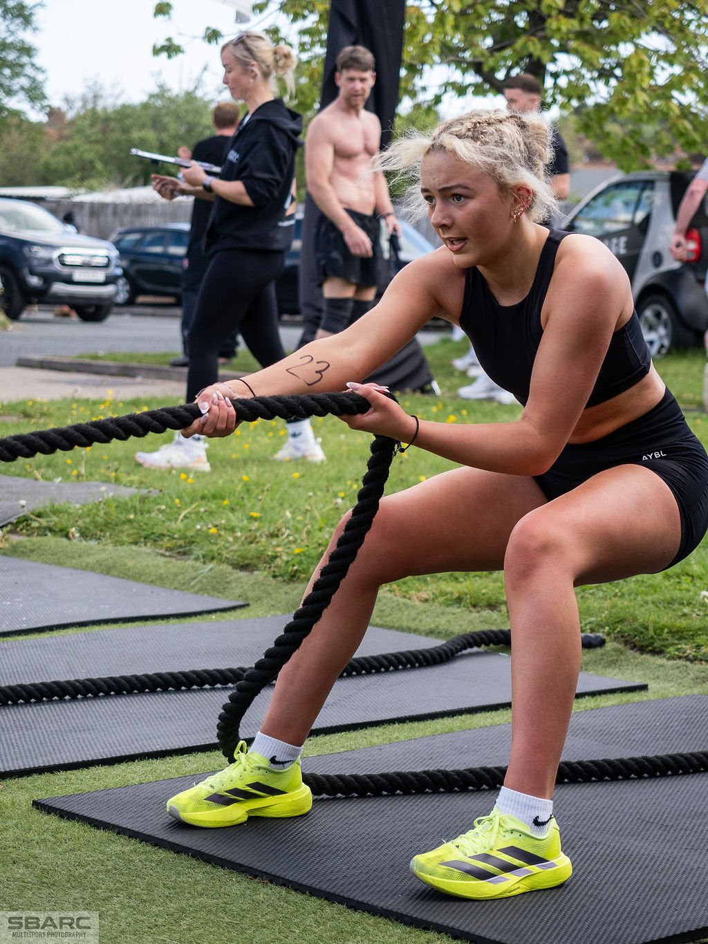 Woman performing a sled pull during a HYROX-style simulation event at a Gateshead gym, pushing through a high-intensity functional fitness workout.